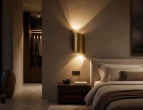 Applique dorata dalla forma curva che proietta suggestivi riflessi luminosi sulla parete di una camera da letto.