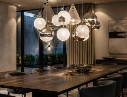 Lampadari scultorei in vetro opalino e argentato sospesi sopra il tavolo di una sala da pranzo contemporanea.
