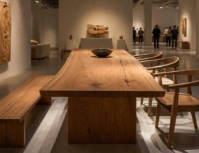 Tavolo scultoreo in legno massello con venature naturali esposto in uno spazio dedicato al design contemporaneo.