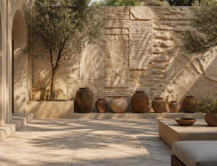 Cortile mediterraneo con parete decorativa, piante in vaso e arredi da esterno.